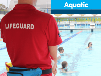 A pool lifeguard standing by the pool watching three people in the water