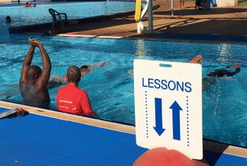 Multicultural men in the pool learning swimming skills with their swim instructor