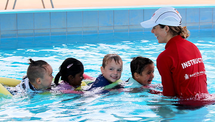 Four children with their swim instructor in the pool on pool noodles