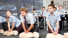 Three school students practicing CPR on a resuscitation manikin