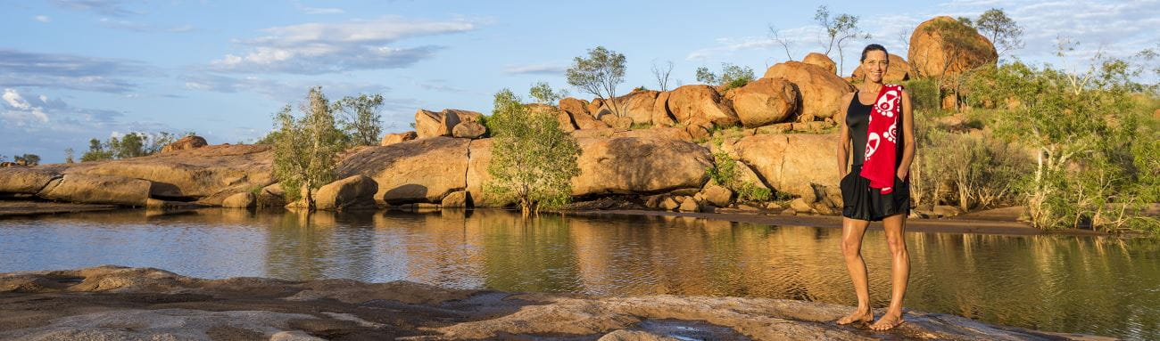 Royal Life Saving WA's Jacqui Forbes with a red Swim and Survive towel over her should standing in front of a Pilbara lake with red rock hills in the background