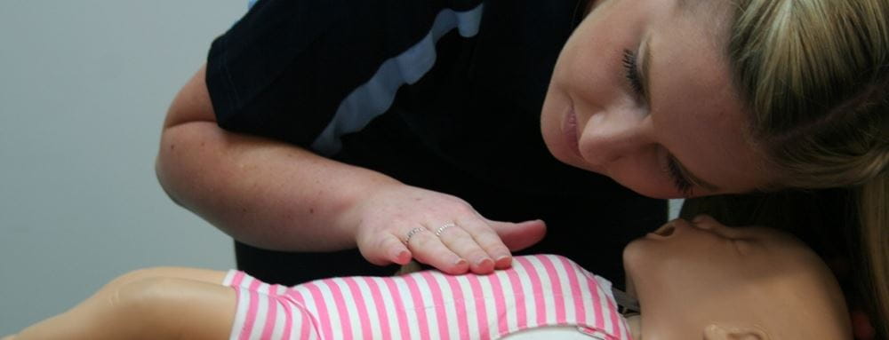 woman checking for breathing in infant manikin