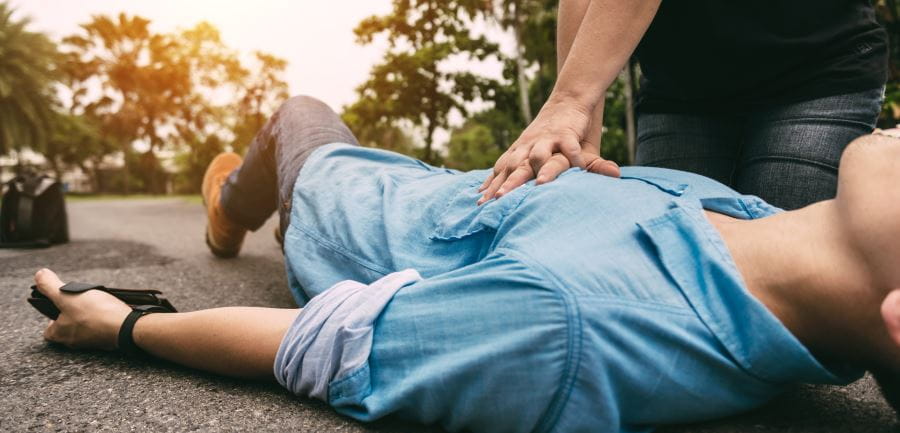 a person laying collapsed on the ground with another person doing CPR