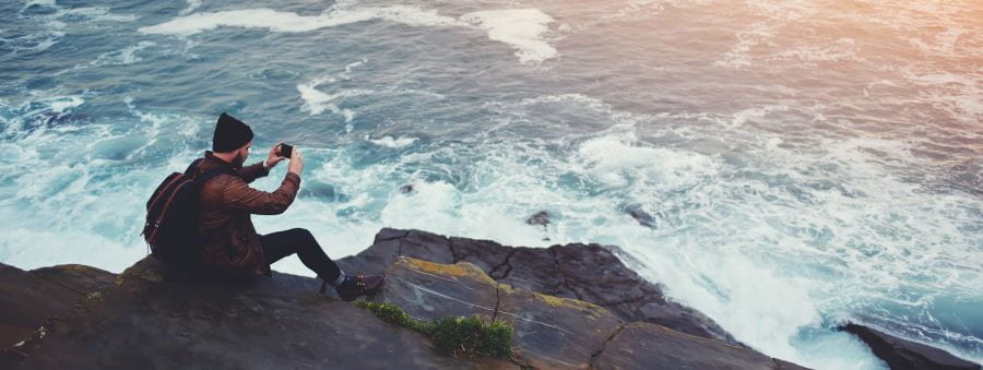 A man sitting on rocks taking a photograph of the water below him