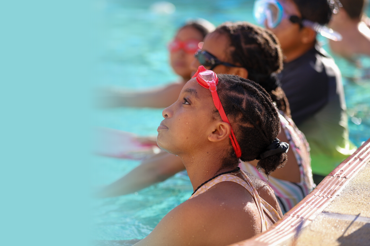 A group of students holding kickboards in the pool look upwards