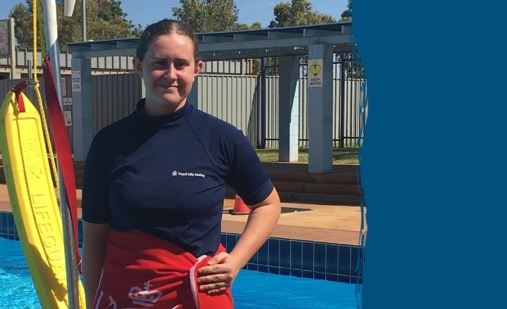 Young woman in a lifeguard shirt standing poolside beside lifesaving gear and signage.