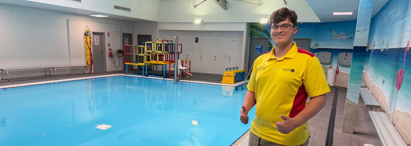 Kaedan [left] wearing lifeguard uniform standing in front of hydrotherapy indoor pool