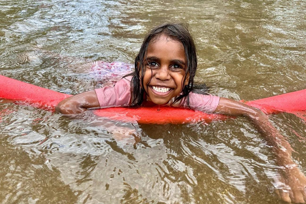 young Indigenous girl floating on a pool noodle in a river