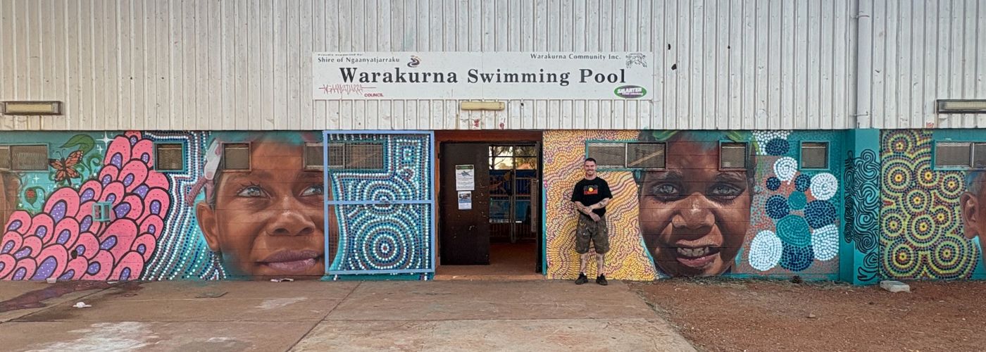 Photo of front of the pool with artist standing in front of mural