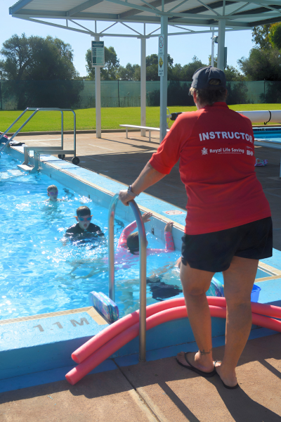 Swim instructor standing on pool edge as children swim freestyle
