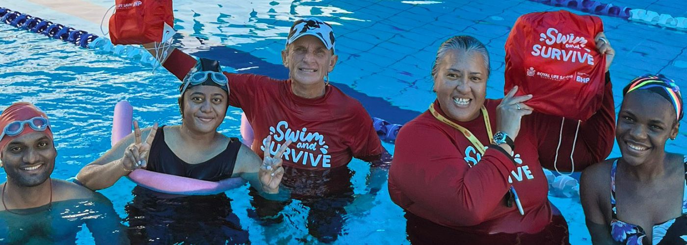 Swimmers and teachers in pool smiling and holding up Swim and Survive packs