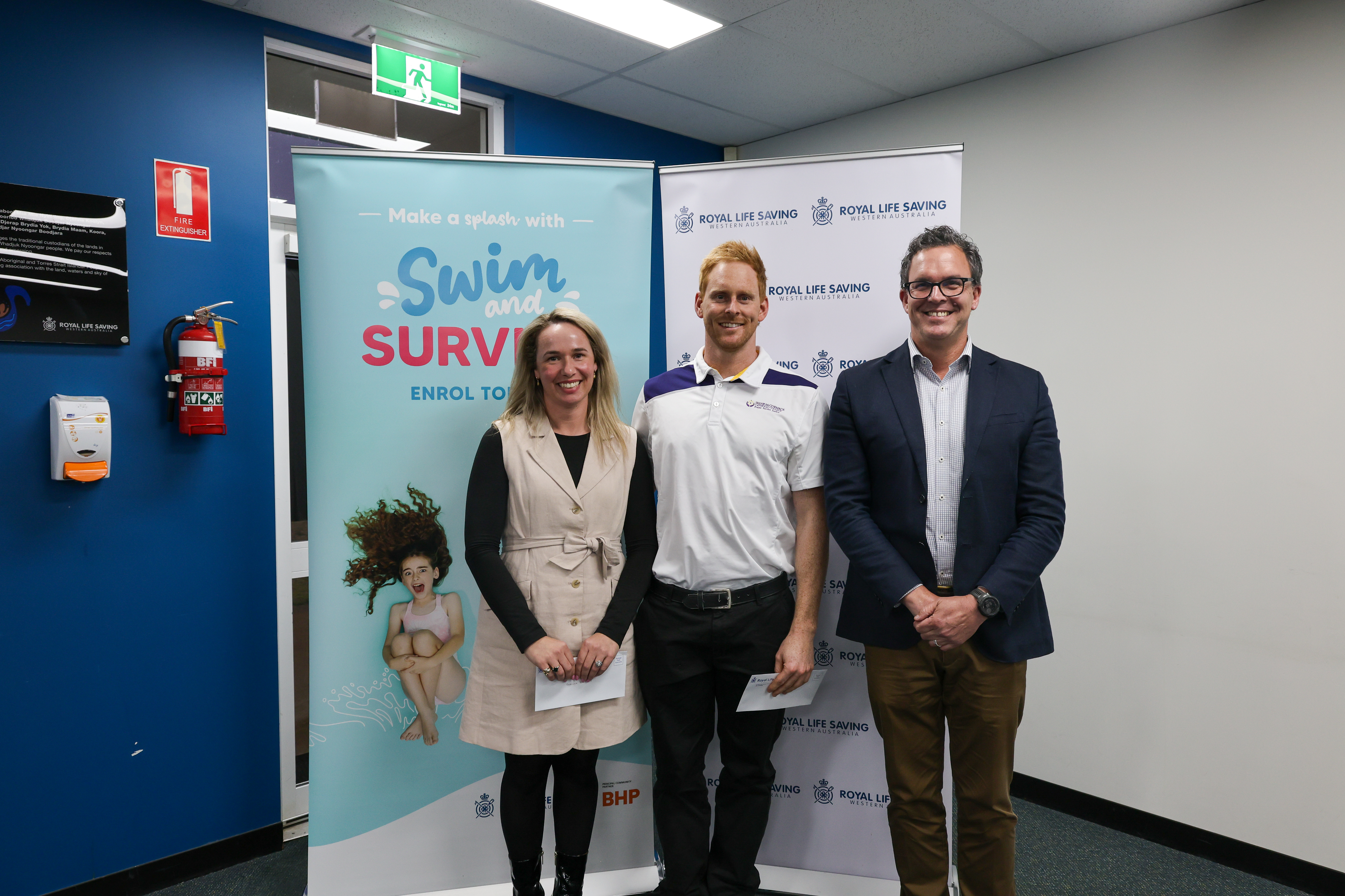 Three attendees smile for a photo in front of Swim and Survive and Royal Life Saving WA banners at the 2026 AGM.