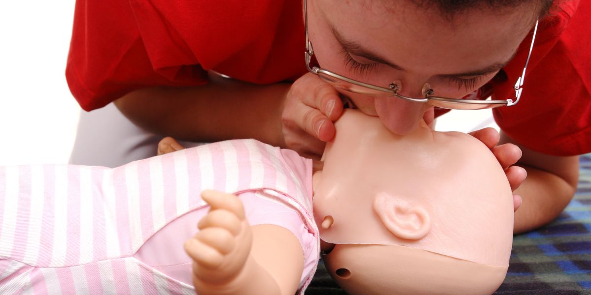Woman wearing glasses giving mouth-to-mouth on infant CPR mannequin
