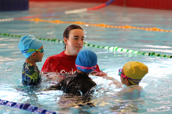 Three young students stand around their teacher in the pool