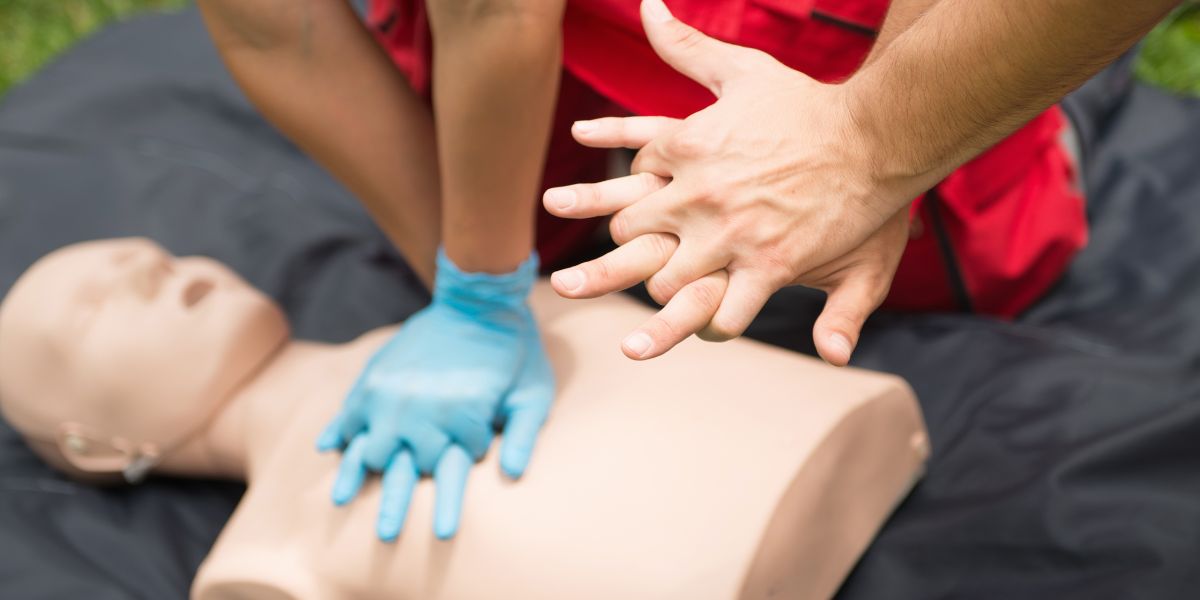 Hands with interlaced fingers hovering above CPR mannequin 