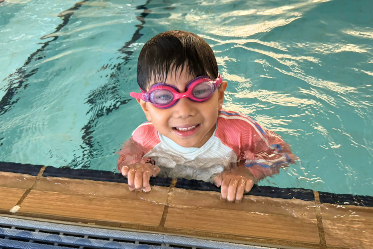 young multicultural boy wearing goggles and smiling in a pool