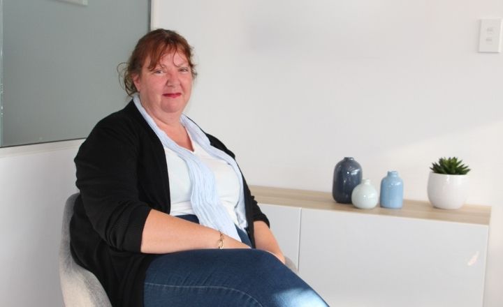 Mother Michelle sitting in grey chair next to a waist height buffet which is holding decorative vases