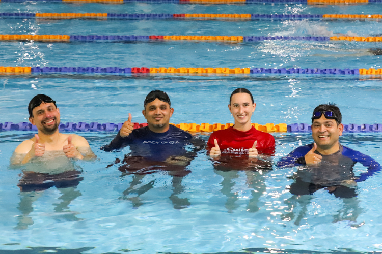 3 participants of a men's only swimming lesson with their instructor in the pool