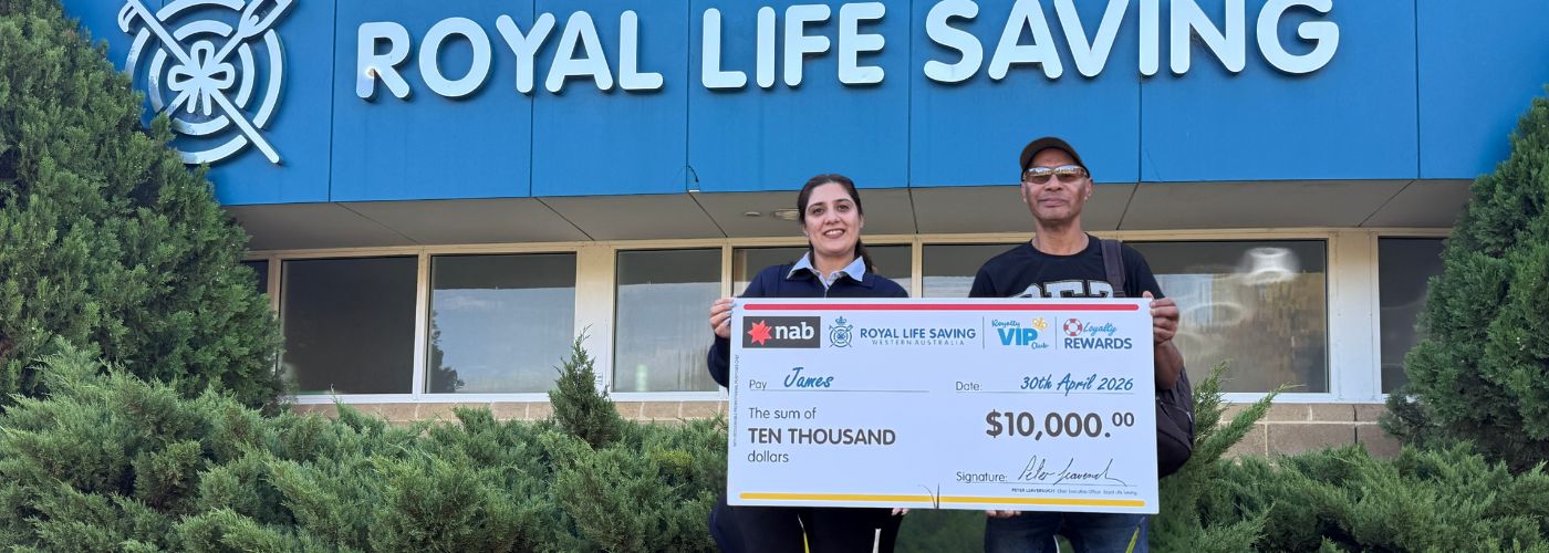 Two people standing holding giant cheque in front of office building