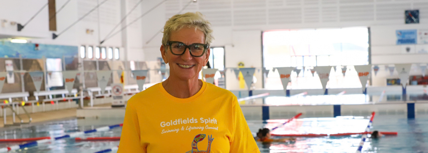 Swimming instructor Di Crisp smiling beside an indoor pool at the Goldfields Spirit Swimming and Lifesaving Carnival.