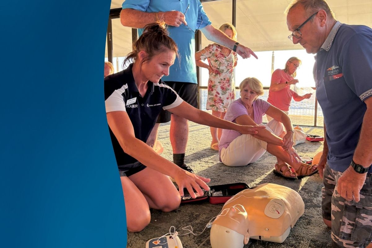 Female CPR trainer on knees next to CPR manikin indicating people to back away for the defibrillator shock