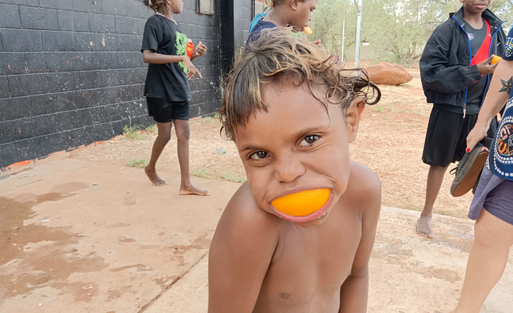 A young boy smiles with an orange peel in his mouth