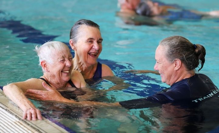 Female aquatic trainer in pool with two elderly women with grey hair training them on water rescue