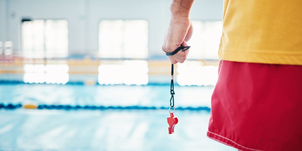 Lifeguard grips whistle with pool in the background