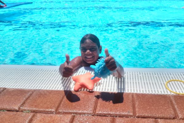 Young aboriginal boy smiling in the pool holding thumbs up to the camera
