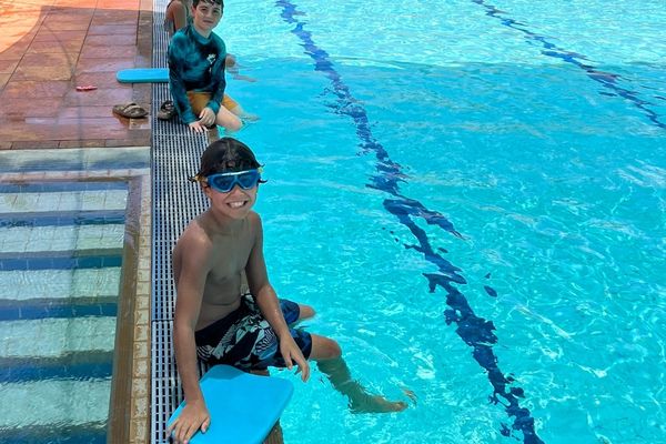 Kid sitting on the edge of the pool smiling at camera