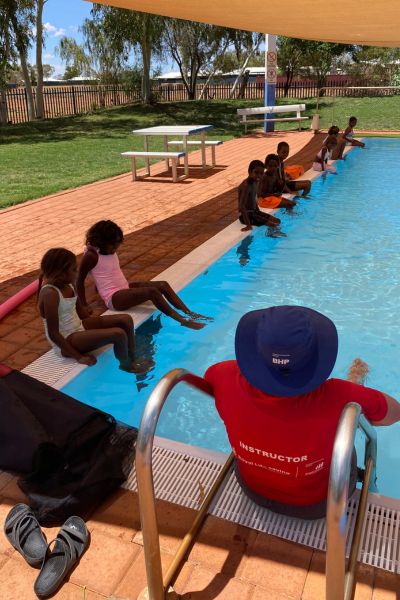 Instructor with back to camera instructing kids on side of the pool