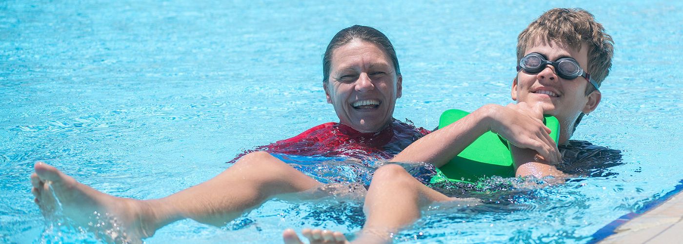 Swimming instructor supporting a child floating on their back with a green flotation aid.