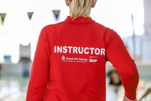 Royal Life Saving swimming instructor in a red uniform standing beside an indoor swimming pool