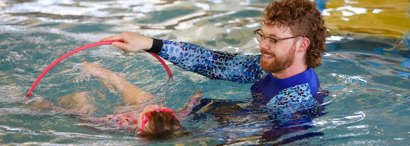 Young girl in pink bathers swimming through hoop swim teacher dressed in blue