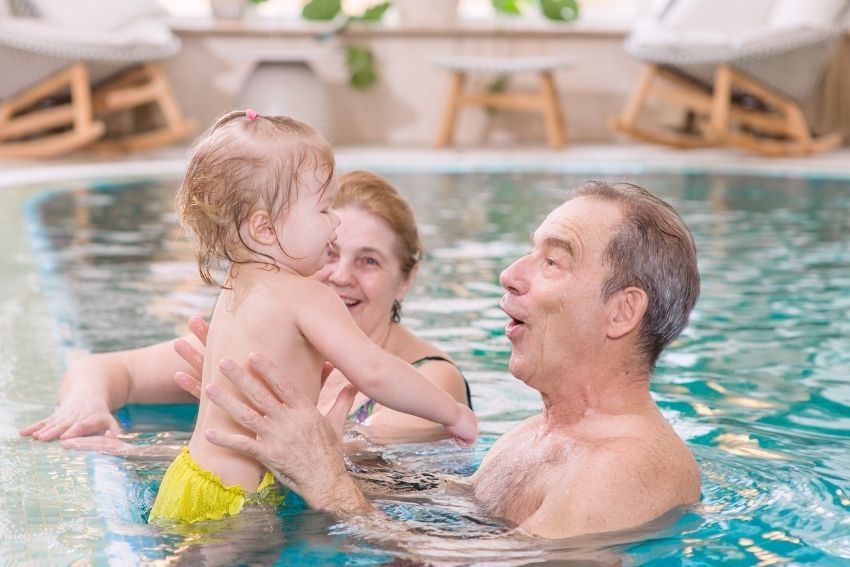 Male and female grandparents in pool holding their toddler grandchild playing and smiling