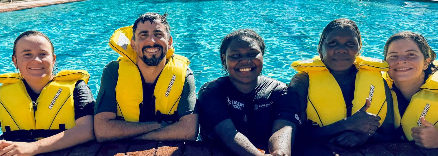 Gen Masa (middle) smiling on the side of pool with newly qualified Bronze Medallion participants