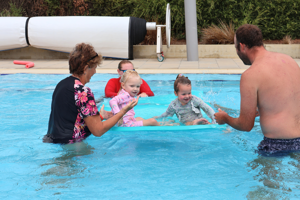 Parents hold their children in the water around a mat the instructor is holding