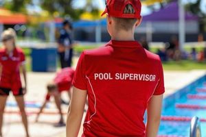 Pool supervisor in a red uniform overseeing activities beside an outdoor swimming pool.