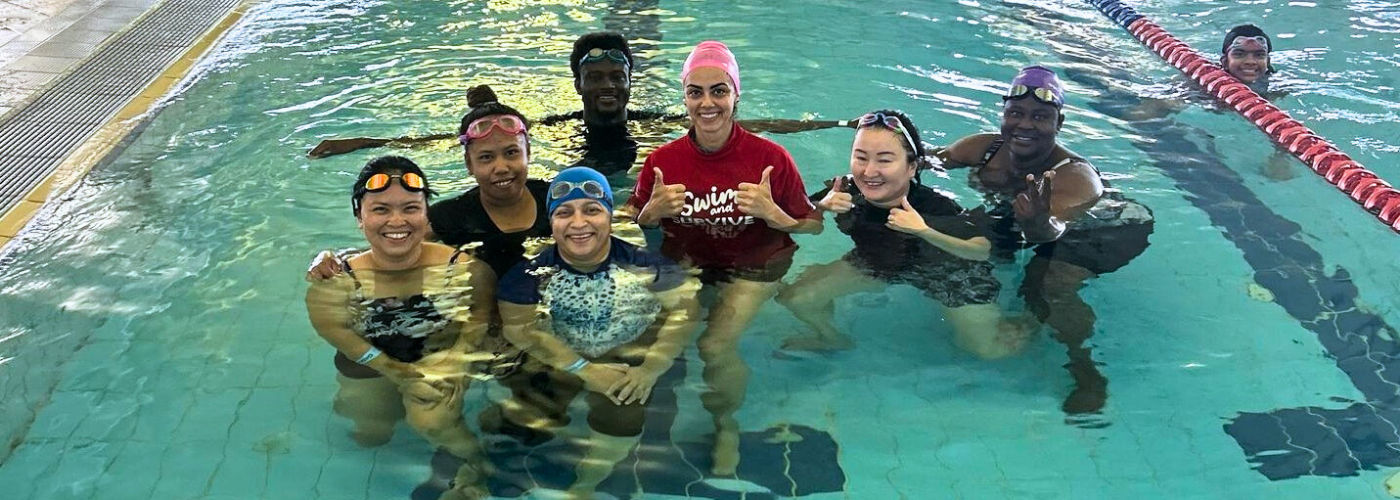 An instructor and adult students give thumbs up in the pool