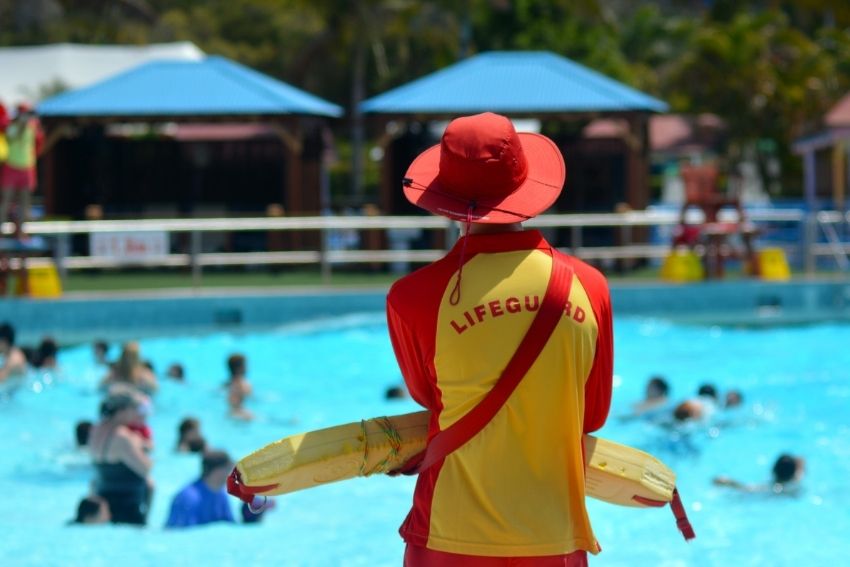 Back of male lifeguard watching over busy outdoor public pool on a sunny day