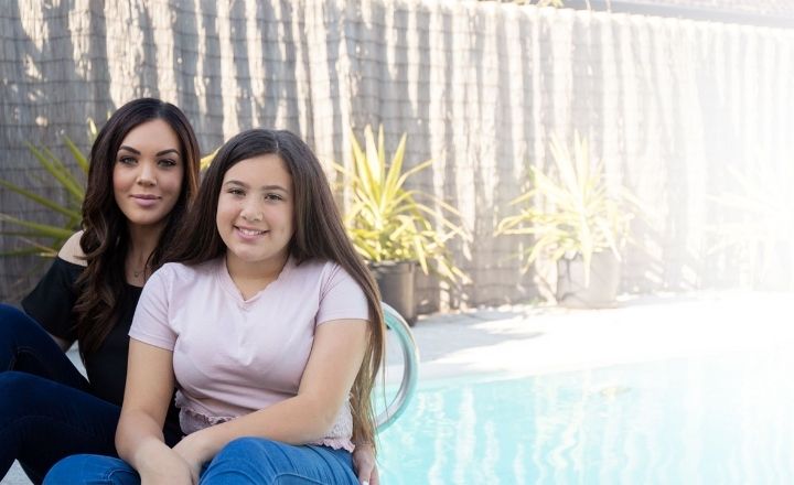 Mother Emma sitting next to 14 year old daughter Mia next to a swimming pool