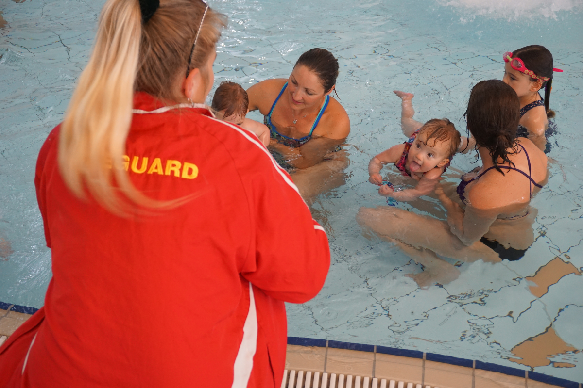lifeguard watching over young children with their carers in a baby pool
