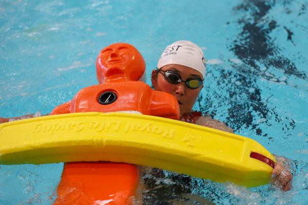 A pool lifesaving competitor tows an orange rescue manikin using a yellow rescue tube.