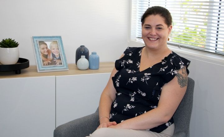 Mother Kylie sitting in black shirt next to a credenza with a photo of her and her child in a frame