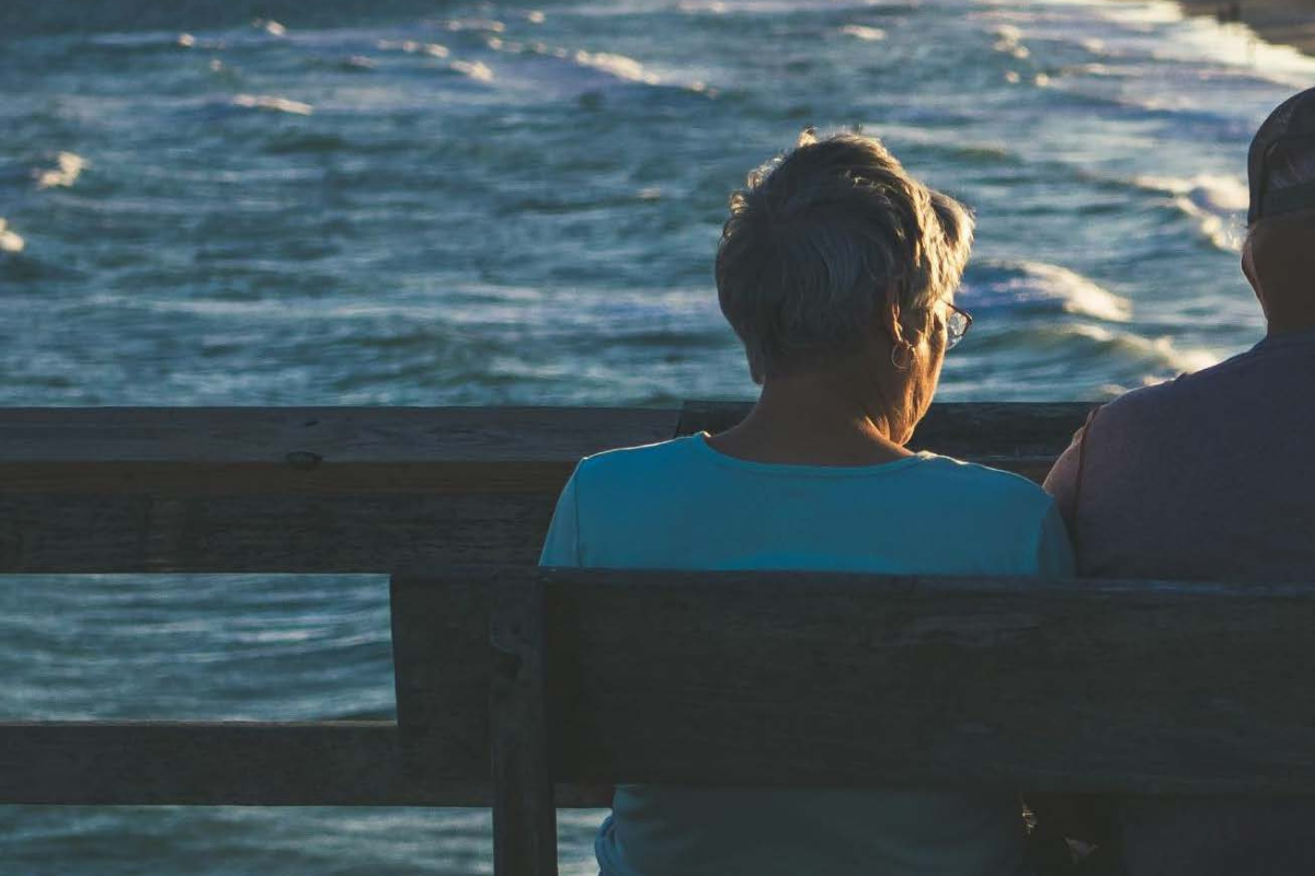 Older woman sits on bench facing the ocean 