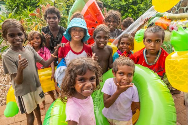 Group photo of children smiling and looking at camera with inflatable fruit pool toys in background