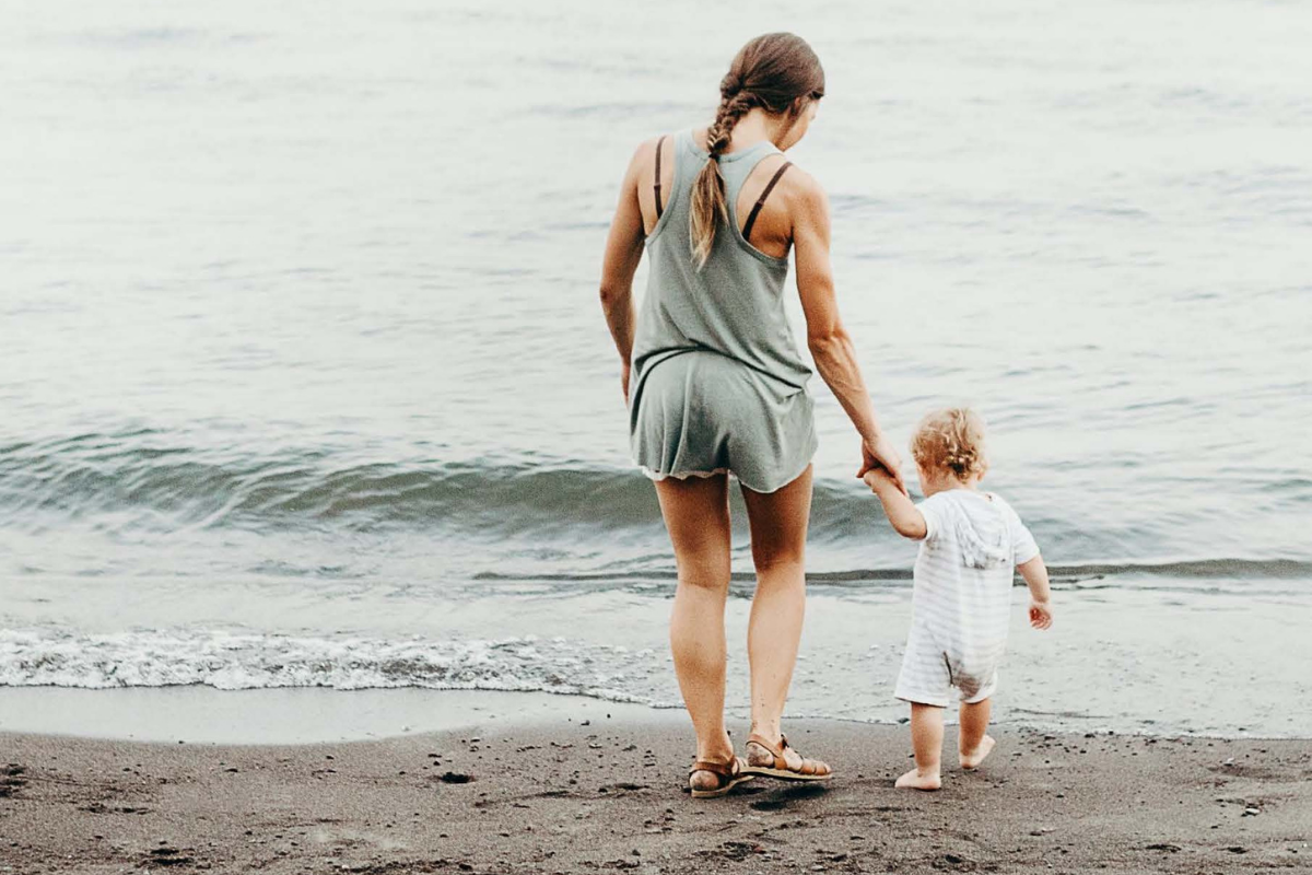 Mother holds child's hand by shoreline