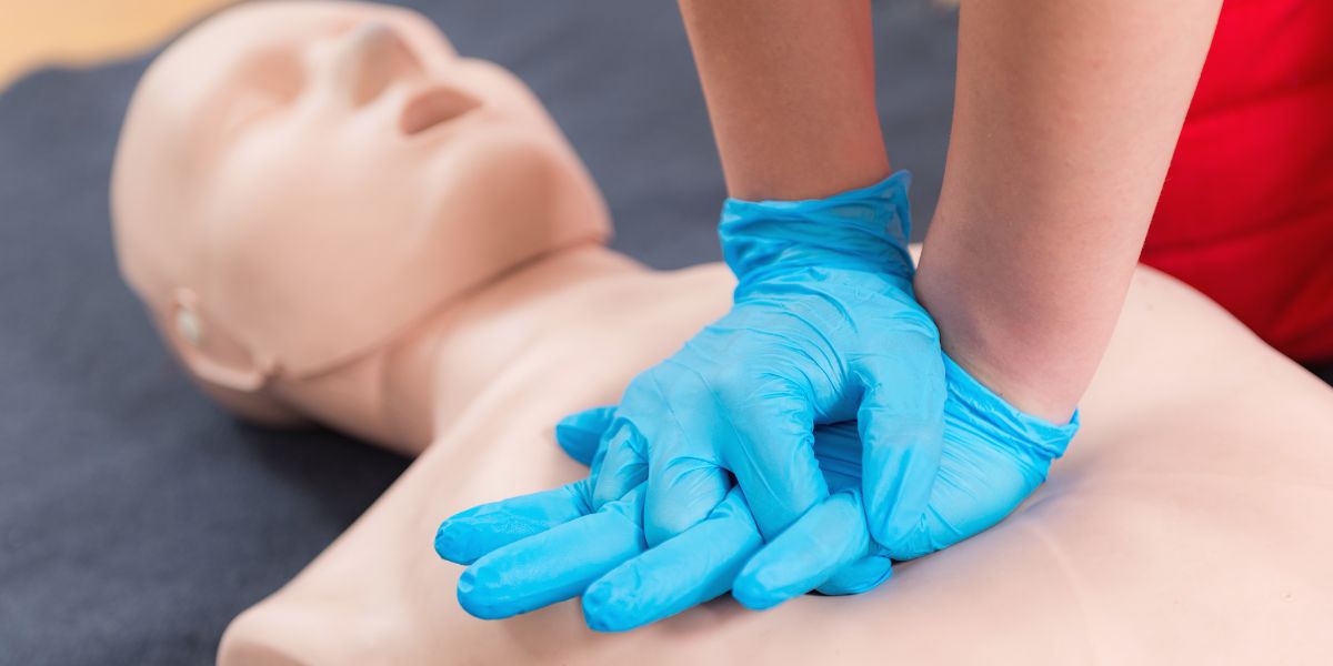 Hands wearing blue gloves performing CPR on a dummy