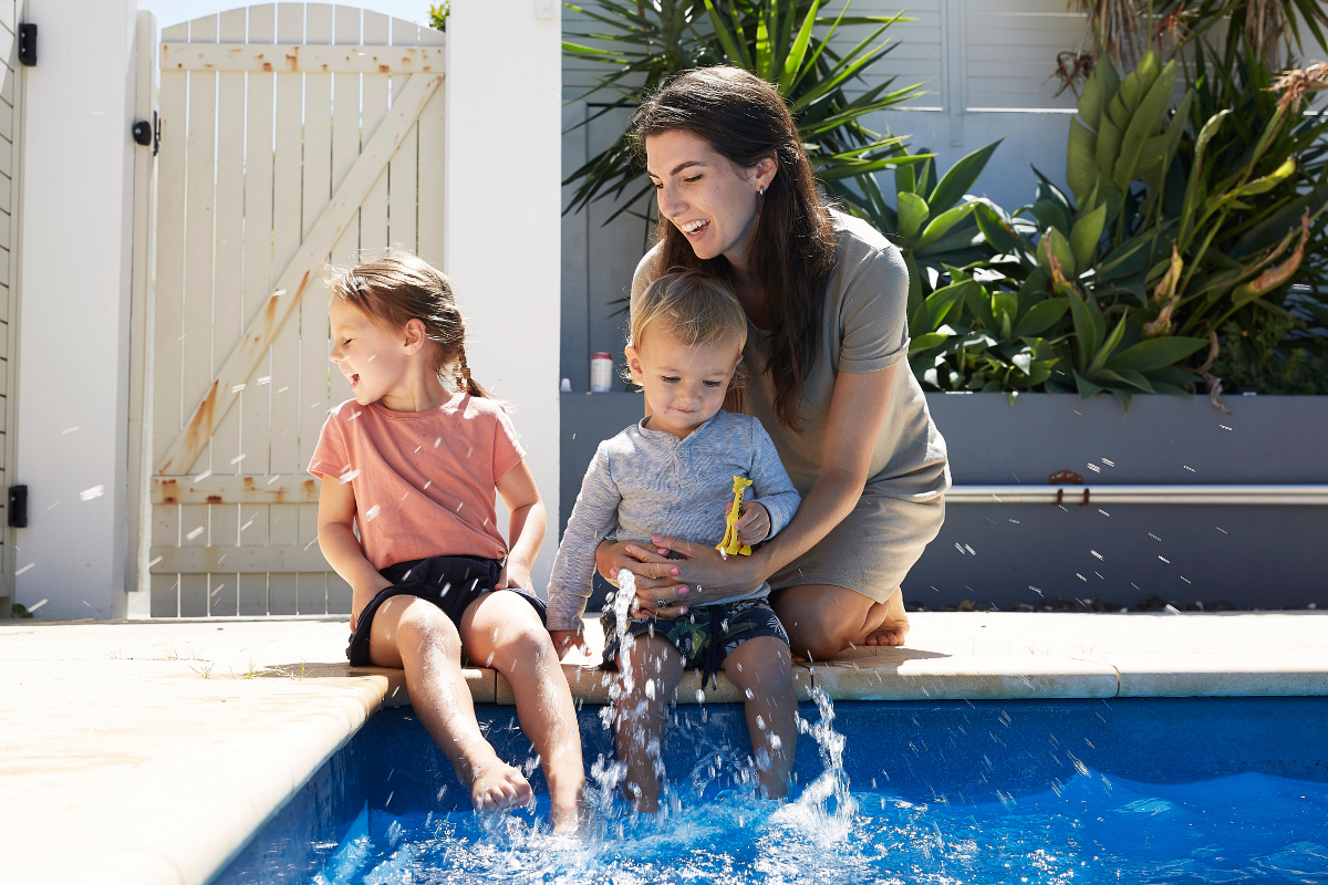 Mother sits and splashes with two young children on pool edge