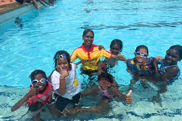 Kids and a lifeguard smile up at the camera from in the pool